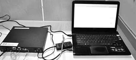 A black UHS-II protocol analyzer box connected via cables to a laptop displaying an analysis interface on its screen.
